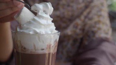 Bir insan uzun bir bardak sıcak çikolataya lokum batırır..