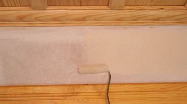 Bir insan sıcak bir iç mekanda rulo kullanarak duvara boya sürüyor..