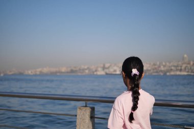 Genç kız nehir kıyısında duruyor, önündeki sakin manzaraya hayran..