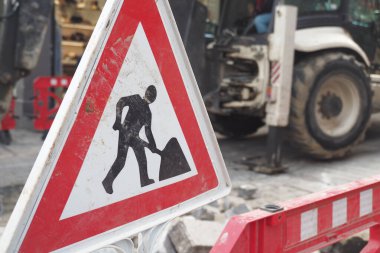 Uyarı levhası işlek bir şehir caddesinde inşaat faaliyetleri olduğunu gösteriyor.
