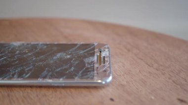 Paramparça bir ekranı olan hasarlı bir akıllı telefon ahşap bir masada oturur..