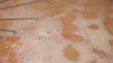 Bir aşçı yemek pişirirken ocakta kaynayan bir çorba kabını karıştırır..