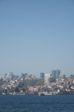 Sakin su, berrak mavi gökyüzüne karşı canlı bir şehrin ufuk çizgisini yansıtır..