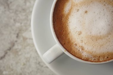 Masadaki beyaz bardakta servis edilen köpüklü sütle kapuçino..