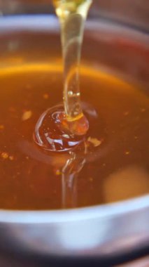 Altın bal yavaşça bir kaşıktan kaseye akar ve dokusunu gösterir..