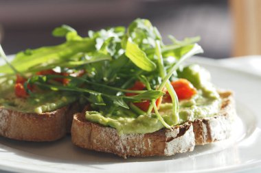 Lezzetli avokado tostu taze roka ve tahıllı ekmeğin üzerinde servis edilir..