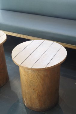 Yuvarlak kapaklı basit ahşap masalar gri bir bankın yanında düzenlenir..