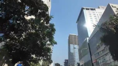 Uzun binalar mavi gökyüzüne karşı ortaya çıkar. Güneş ışığı camlardan yansımaktadır..