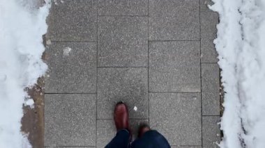 Kış boyunca karlı kaldırımda kahverengi çizmeler giyerek yürüyen bir insan..