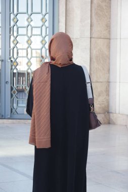 Geleneksel kıyafetler giyen bir kadın binanın girişinde sessizce durur..