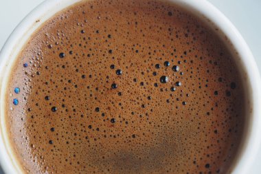 Yüzeydeki bir fincanda köpüklü baloncukları gösteren koyu kahvenin yakın görüntüsü.