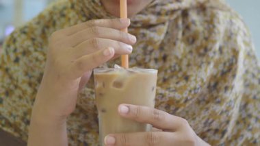 Bir insan anın tadını çıkarırken, elinde buzlu içecekle dolu bir bardak tutar..