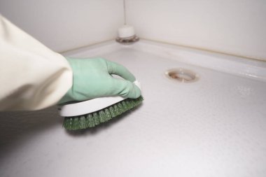 Bir kişi yeşil eldiven ve fırça ile duş yüzeyi fırçalar..