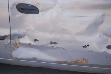 Gümüş renkli bir araba kapısında yüzeyde belirgin çizikler ve pas var..