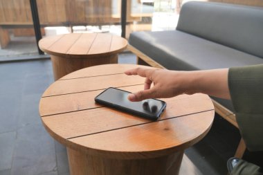 Bir el, kafedeki ahşap bir masada dinlenen akıllı telefona doğru uzanır..