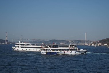 Arka planda bir köprü olan iki tekne denizde yüzüyor..