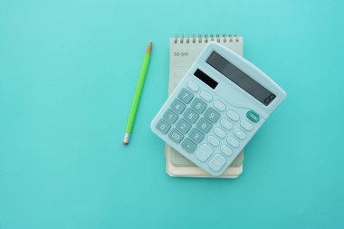 Bir hesap makinesi yanında bir kalemle not defterlerinin üzerinde duruyor..