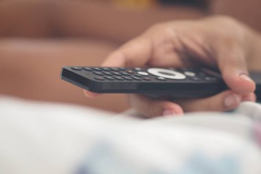 Bir insan en sevdiği programı izlemek için uzaktan kumandayı tutar..