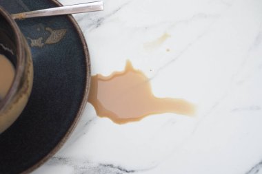 Kahverengi kahve bir fincan ve çay tabağının yanında mermer bir yüzeye dökülmüş..