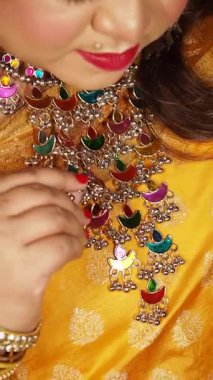 Bir kadın parlak sarı bir elbise giyerken karmaşık mücevherleri ön plana çıkarıyor..