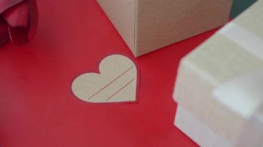 Kalp şeklinde bir not, paketlenmiş hediyelerin yanında parlak kırmızı bir arka plana dayanır..