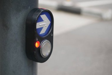 Yayalar bir kavşakta karşıdan karşıya geçmek için bekler, sinyal düğmesi görünür.