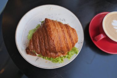 Kruvasan bir tabakta, kafede bir fincan kahvenin yanında duruyor..