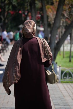 Uzun elbiseli ve fularlı bir kadın güneşli bir günde parkta geziniyor..