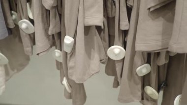 Perakende mağazasında güvenlik etiketli bej t-shirtler asılı..