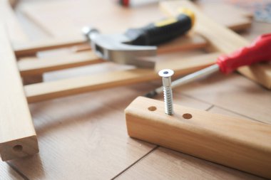 Çeşitli aletler montajı bekleyen ahşap mobilya parçalarının yanında yatıyor.