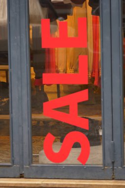 Parlak kırmızı satış tabelası gün ışığında dükkan vitrinine dikkat çekiyor.