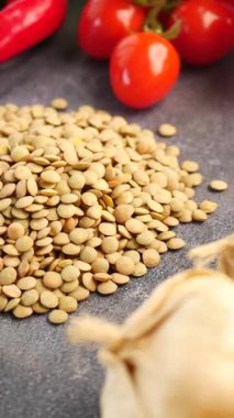 Mercimek gri bir yüzeye serpilmiş, yanında taze domates ve sarımsak var..