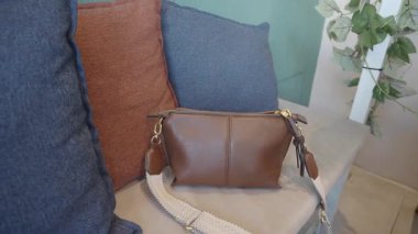 Şık bir kahverengi çanta, kapalı alandaki yastıkların üzerinde dinlenir..