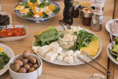 Çeşit çeşit peynir, yeşillik ve zeytin, ahşap masa düzeninde..