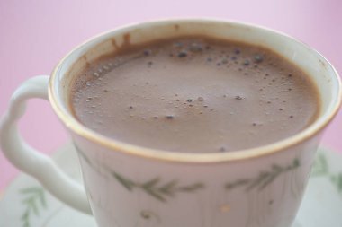 Pembe arka planda duran sıcak çikolata dolu dumanı tüten bir fincan..