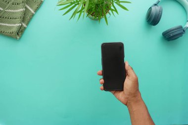 Bir el, bitkilerle dolu canlı bir masanın üstünde siyah bir akıllı telefonu tutuyor..