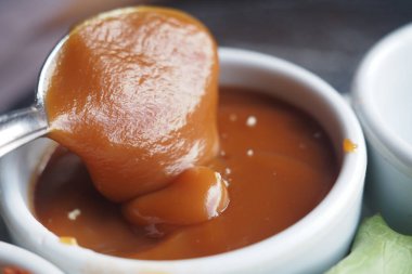 Kalın karamel sosu bir tabakta parıldıyor ve kaşığı kenarda duruyor..