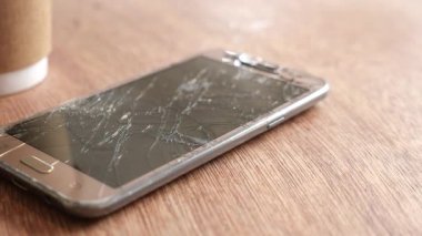 Hasarlı bir akıllı telefon, kahve fincanının yanındaki ahşap bir masada yatıyor..