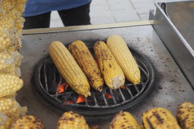 Taze mısırlar, hareketli bir pazarda açık bir alevin üzerinde kızartılıyor..