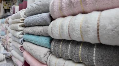 Müşteriler, düzgün istiflenmiş havluların bulunduğu canlı bir market tezgahına bakıyorlar..