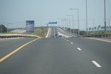 Uzak palmiye ağaçları ve açık gökyüzü olan geniş bir otoyolda araçlar.