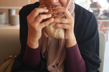 Bir kadın sandviçi tutar ve kafeteryada bir ısırık alır..