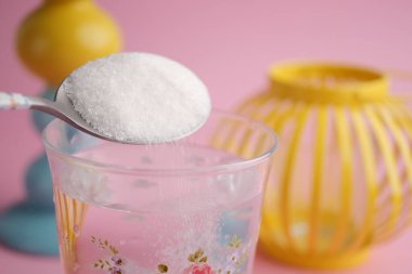 Parlak dekorun yanındaki bir bardak suya bir kaşıktan şeker dökerek..