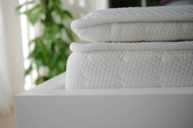 Temiz bir şekilde düzenlenmiş beyaz yatak, kapalı bir yerde düzgün bir yatak çerçevesi üzerinde dinleniyor..