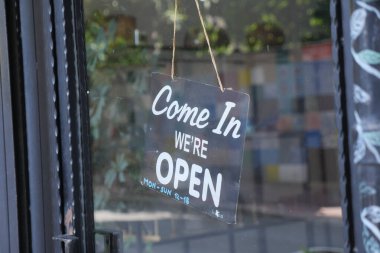 Bir karşılama tabelası gündüz bir mağazanın açık durumunu gösterir.