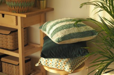 Çeşitli renklerde yumuşak yastıklar bir saksı bitkisinin yanındaki tahta bir taburede dinleniyor..