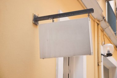 Duvarda boş bir tabela asılı, sakin bir sokak atmosferiyle çevrili..