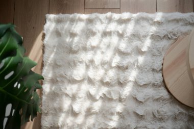 Güneş ışığı yeşil bir bitkinin yanındaki tüylü bir halıya desenli gölgeler bırakır..