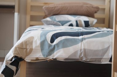 Yumuşak desenli yatak, sıcak bir odada basit bir ahşap yatağı kaplıyor..