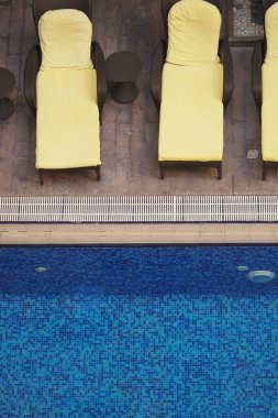 Sarı şezlonglar bu ortamda canlı bir mavi yüzme havuzunun kenarında..